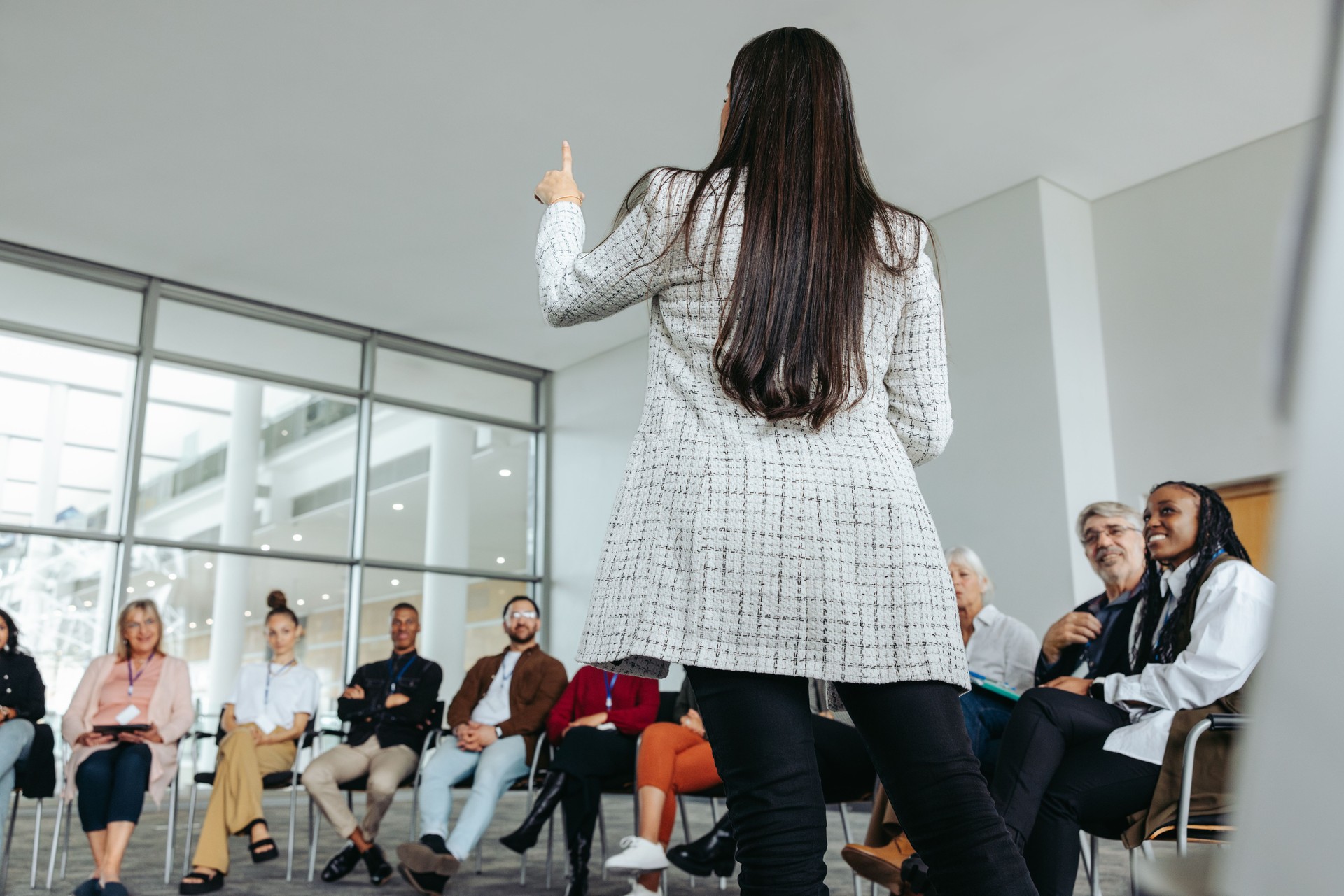Female speaker leading motivational seminar for diverse group in modern conference room